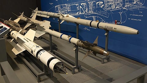Several air-to-air missiles are displayed on stands in a museum setting, with a technical blueprint diagram visible in the background.