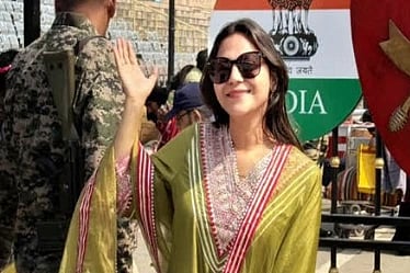A woman in a green traditional outfit and sunglasses waves cheerfully near an Indian flag display. A soldier stands nearby, adding a patriotic context.