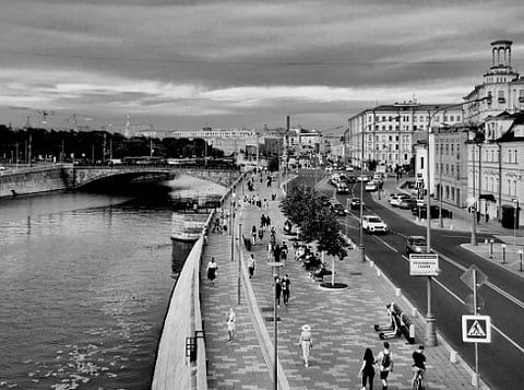 Black and white view of the bustling Moscow River walkway showcasing urban life.
