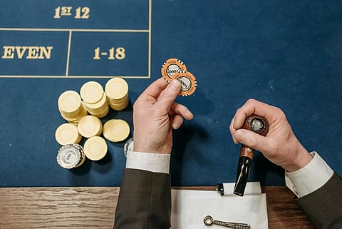 Person holding poker chips and a pipe over a casino table with chips neatly stacked; a sense of anticipation and strategy is conveyed.