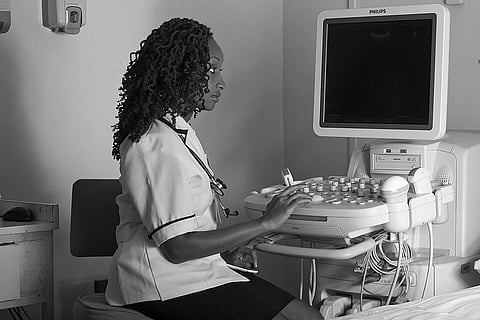 A healthcare professional in a uniform operates an ultrasound machine in a medical setting, focused and attentive. The atmosphere is calm and clinical.