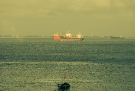 Serene ocean view with a fishing boat and distant cargo ships under a cloudy sky. The image has a yellowish tint to it. 