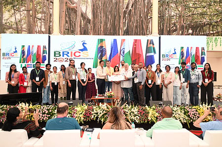 In the image the BRICS 2026 is shown in which many people with i card are shown standing on the stage