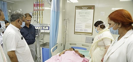 In the image a hospital seen is shown with a women lying in the bed while the other wearing mask are watching her