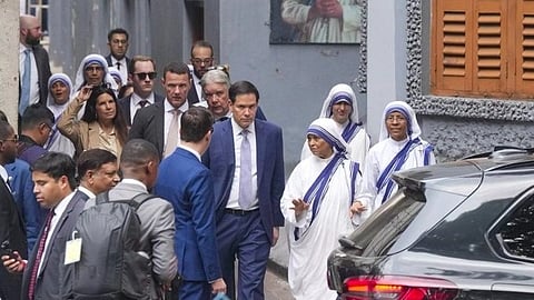 A group of people, including Marco Rubio and nuns in white and blue habits, walk through a narrow street. A portrait of Mother Teresa is visible on the wall.