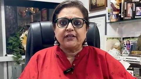 A woman with glasses is seated at a desk, sipping from a coffee mug while engaged in her tasks.
