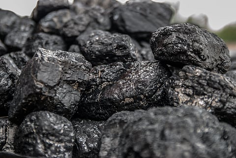 Close-up of a pile of shiny black coal lumps. The irregularly shaped pieces are stacked together, highlighting their rough texture and glossy surfaces.