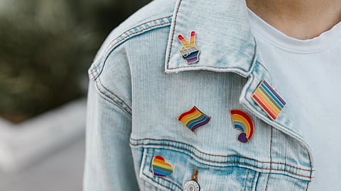 In the image a demin jacket colar is shown wore by a man in the collar different shaped rainbow batches are shown