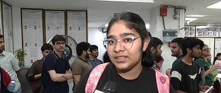 In the image many students are shown standing in a line while one girl is speaking to a media reporter