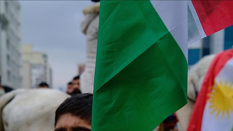 A child with glasses, wearing a black and white scarf, passionately points while holding a flag. There is a festive atmosphere with flags and people in the background.