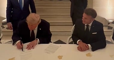 Image of Donald Trump signing US iran deal in France. he is seated next to french president Emmanuel Macron. 