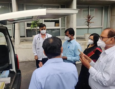 Image of a few people standing behind a van which is opened from behind. there is a doctor present at the scene. 
