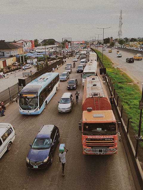 A bustling urban road with diverse vehicles including buses, cars, and trucks during the day.
