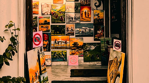 A warmly lit archway showcases a variety of colorful paintings on either side of the entrance, creating a vibrant and inviting artistic display.