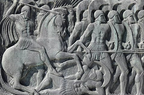 Stone relief depicting ancient warriors in armour; a mounted soldier on horseback leads, while others wield spears in a dynamic battle scene.