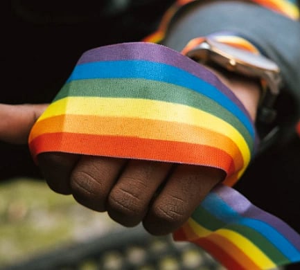 A hand wrapped in a rainbow-striped ribbon symbolizes LGBTQ+ pride. The vibrant colors convey support and solidarity, evoking a sense of unity and acceptance.