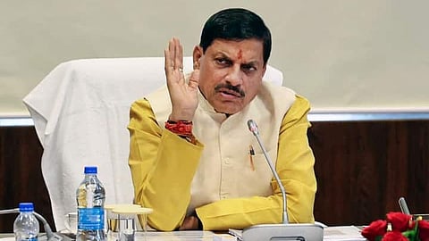 MP CM Mohan Yadav sitting on a chair, speaking on the mic lying on the table in front of him.