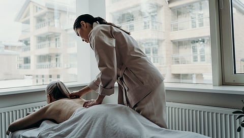 A massage therapist gives a back massage to a client in a serene room with large windows overlooking modern buildings, conveying relaxation and care.