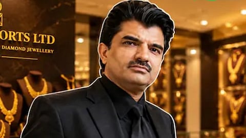 Rajesh Mehta wearing black suit, shirt, and tie with his Rajesh Exports Jewelry shop in the background.