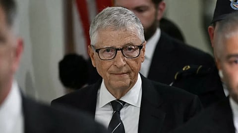  Bill Gates seen walking through a corridor, wearing a suit and appearing engaged in thought.