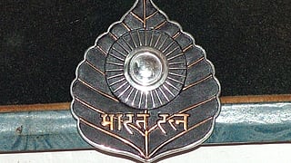 A Bharat Ratna medal with a peepal leaf shape, central sunburst design, and a silver emblem. The script "भारत रत्न" is inscribed below.