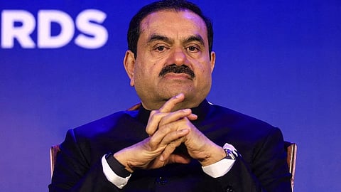 Gautam Adani at an event with blue background and pensive look on face.