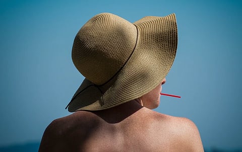 A woman with a wide-brimmed hat enjoys a sunny day at the beach with a drink in hand.