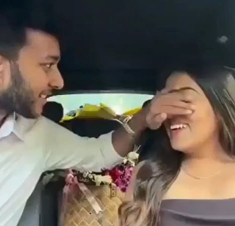 Image of Ketan Agarwal and Siya Goyal n a car. ketan is covering his fiancée's eyes to gift her flowers. 