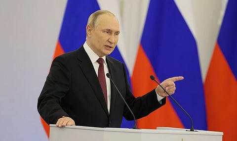 Image of Vladimir Putin during a speech at the annexation ceremony. he has raised his left hand and is standing in front of a podium. 
