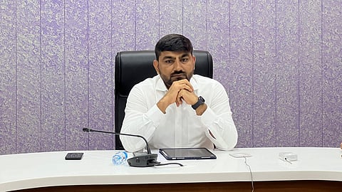 IAS Officer Rajendrakumar Patel sitting at collector's desk in white shirt with mic and other digital devices on the dest.