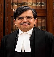 Image of former judge S. Muralidhar in his official uniform. he is standing in front of  a book shelf. 