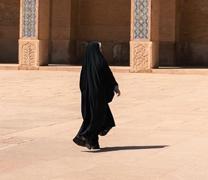 A woman in traditional attire walking by a beautifully decorated mosque on a sunny day.
