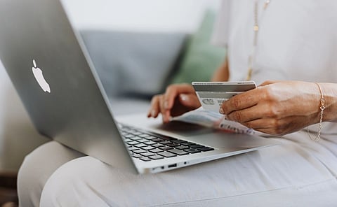 Close-up of a person holding a credit card while shopping online using a laptop at home.
