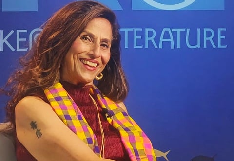 Image of columnist Shobhaa De smiling and looking towards the camera. Behind her is a blue background with text such as literature written on it.