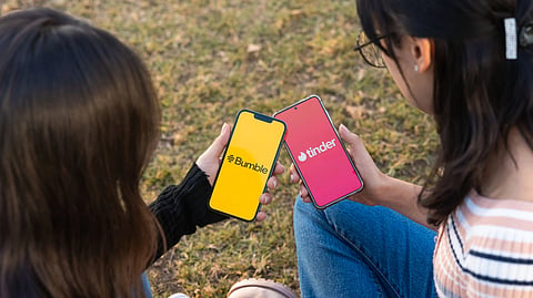 Photo showing two women, with dating apps Bumble and Tinder open on their phones