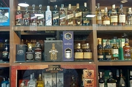 Image of numerous bottles of liquors placed on a wooden shelf with glass doors. 