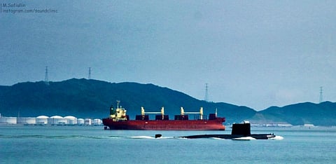 image of a submarine coming up from the ocean. another cargo ship is visible behind the submarine