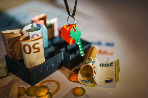 Image shows a key a house keychain and money in paper currency and coins.