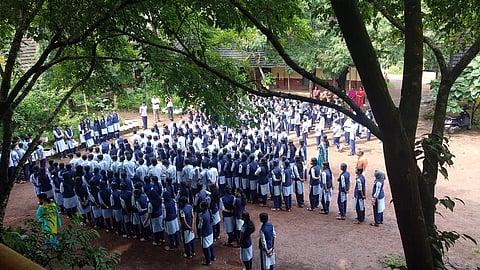 A school assembly where many children are shown standing in the ground for morning prayer
