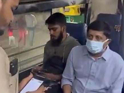 Image of Karnataka transport minister Byrathi Suresh sitting on BMTC bus. his face is covered with a mask and he is seated in front of a bus conductor. another passenger is sitting beside him.
