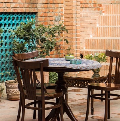 A charming outdoor patio with wooden chairs and a table set against a brick wall, adorned with plants.