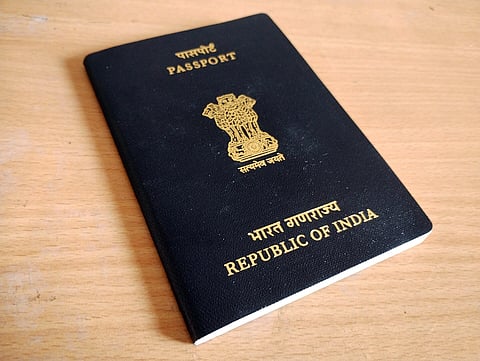 Black Indian passport on a wooden surface, showing the national emblem and "Republic of India" printed in gold.