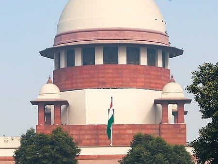 Image of supreme court of India. The top court along with trees and Indian flag is visible in the image. 