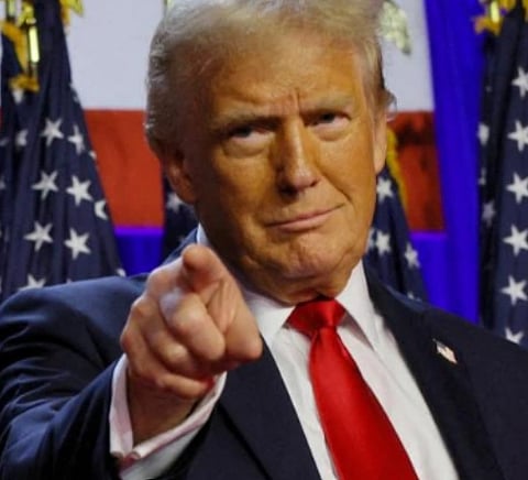Image of Donald Trump pointing his finger towards some direction. he is smirking and behind himare the flags of USA. 