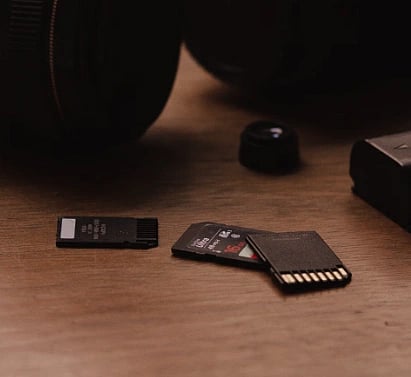 Close-up of camera lenses and SD cards on a wooden surface.