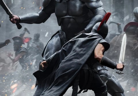 Official poster of Christopher Nolan's The Odyssey in which a man in heavy armour is holding a sword and fighting against another man who is twice his size. 