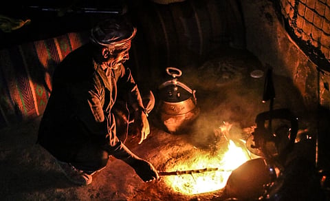 A man tending a fire in a traditional Afghan setting, illustrating rural life and hospitality.
