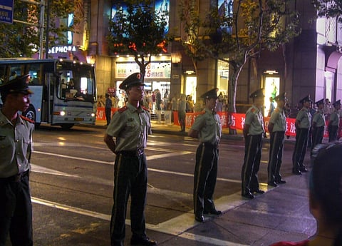 Image of Chinese police blocking the road at Shaanxi Nan Lu. In theimage the police are standing on the road at equal distance and the picture is taken at night. 