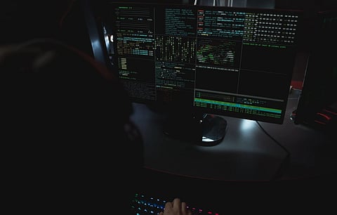 Dark room setup with code displayed on PC monitors highlighting cybersecurity themes.
