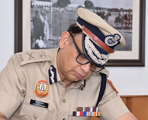 Image of Anurag Kumar delhi police commissioner in official uniform writing something. behind him a black and white photo can be seen.